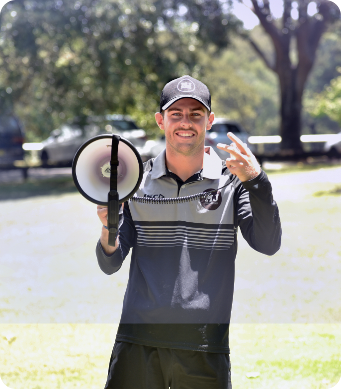 Edge founder Mac Jenkins standing outdoors in a park, smiling and holding a megaphone, wearing a cap and a black-and-gray athletic top.